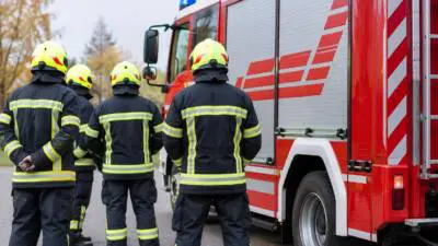 KI-Symbolbild: Personen in Schutzkleidung neben einem roten Einsatzfahrzeug.