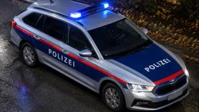 KI-generiertes Bild: Ein silberner Kombi mit blau-roten Streifen und leuchtendem Blaulicht auf nasser Straße.