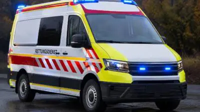 KI-generiertes Bild: Ein weißer Rettungswagen mit gelben und roten Streifen steht auf nasser Straße.