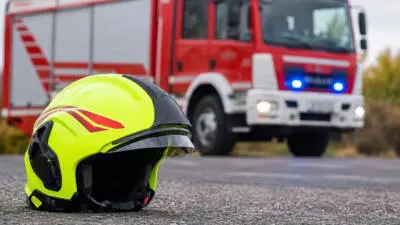 KI-Symbolbild: Ein leuchtend gelber Schutzhelm liegt vor einem roten Einsatzfahrzeug.
