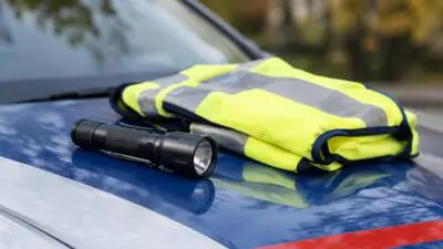 KI-generiertes Bild: Eine Warnweste und eine Taschenlampe liegen auf der Motorhaube eines blau-weißen Fahrzeugs.