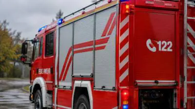 KI-generiertes Bild: Rotes Feuerwehrfahrzeug mit eingeschaltetem Blaulicht auf nasser Straße.