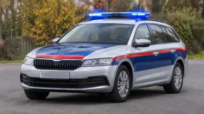 KI-Symbolbild: Ein silberner Kombi mit blau-roter Beklebung und blauem Lichtbalken steht auf einer Straße.