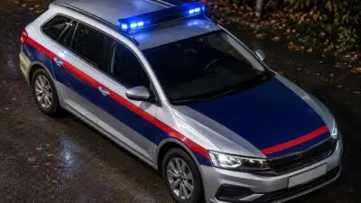 KI-Symbolbild: Ein silberner Kombi mit rot-blauer Lackierung und blauem Lichtbalken steht auf nasser Straße.