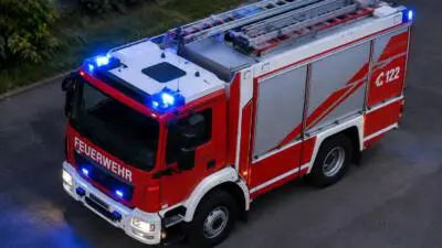 Rotes Feuerwehrfahrzeug mit blauen Warnleuchten, Dachleitern und weißen Seitenflächen auf einer Straße