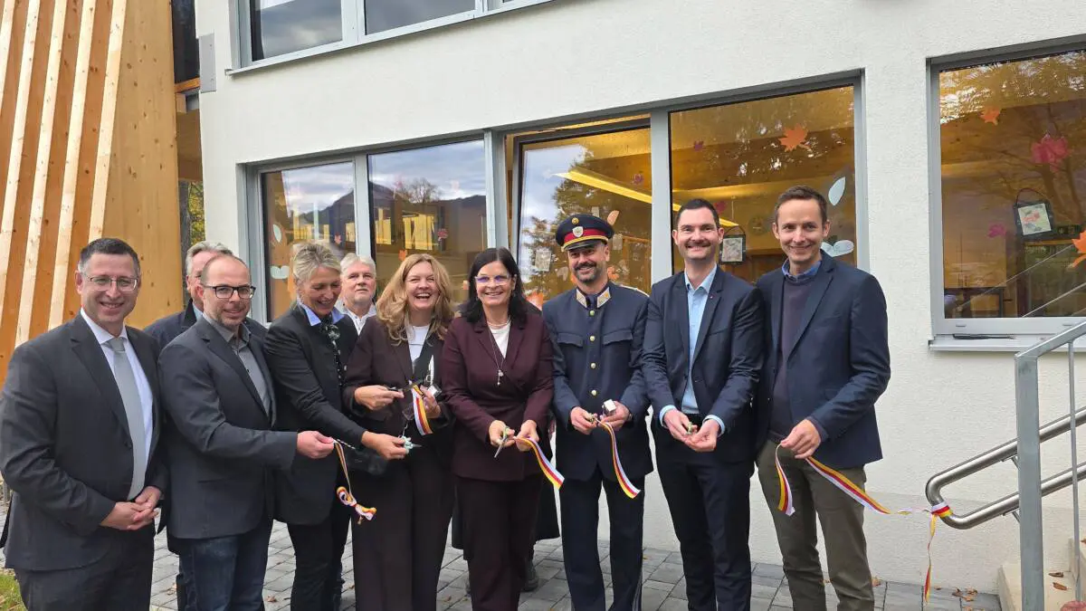Erwachsene stehen mit Scheren und rot-gelben Bändern vor einem Gebäude.