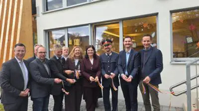Erwachsene stehen mit Scheren und rot-gelben Bändern vor einem Gebäude.