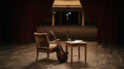 KI-generiertes Bild: Ein Sessel, eine Gitarre und ein Mikrofon stehen auf einer Theaterbühne.