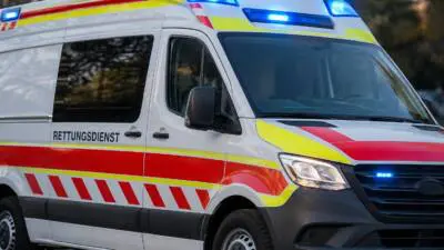 KI-generiertes Bild: Ein weißes Einsatzfahrzeug mit rot-gelben Markierungen und eingeschaltetem Blaulicht.