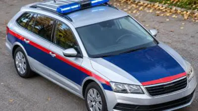 KI-generiertes Bild: Ein silberner Kombi mit rot-blauer Beklebung und blauem Warnlicht auf einer Straße.