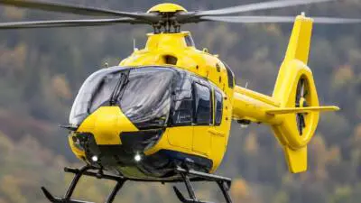 KI-generiertes Bild: Ein gelber Hubschrauber vor unscharfer bewaldeter Berglandschaft.