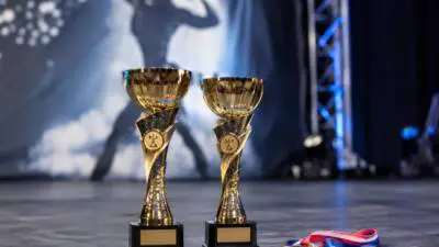 KI-Symbolbild: Goldene Pokale und eine Medaille auf einer Bühne vor einer Kraftsport-Silhouette.