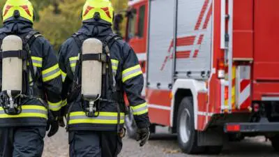 KI-generiertes Bild: Feuerwehrleute in Schutzkleidung mit Atemschutz stehen vor einem roten Löschfahrzeug.