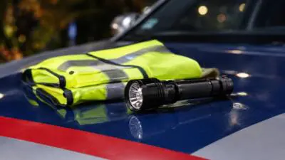 KI-generiertes Bild: Eine gelbe Warnweste und eine Taschenlampe liegen auf einem blauen Fahrzeug.