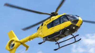 Ein gelber Hubschrauber fliegt vor blauem Himmel mit vereinzelten Wolken.