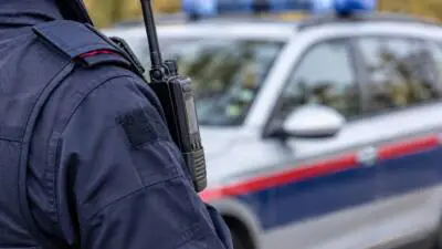 KI-Symbolbild: Dunkelblaue Uniform mit Funkgerät vor einem unscharfen weiß-blauen Fahrzeug.