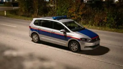 KI-Symbolbild: Ein silberner Kombi mit blau-roten Streifen und Blaulichtbalken steht nachts auf einer Straße.