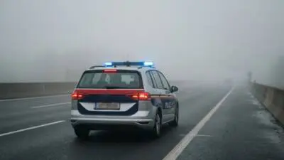 KI-generiertes Bild: Ein Polizeiauto mit eingeschaltetem Blaulicht auf einer Straße im Nebel.