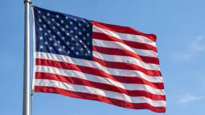 KI-Symbolbild: Eine US-Flagge weht vor blauem Himmel.