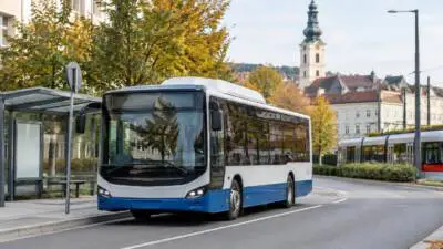 KI-Symbolbild: Ein blau-weißer Linienbus steht an einer Haltestelle vor Stadthäusern.