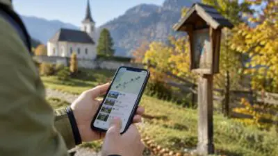 KI-Symbolbild: Hände halten ein Smartphone mit Kartenansicht vor einer kleinen Kirche und einem Bildstock.