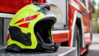 KI-generiertes Bild: Ein neongelber Schutzhelm liegt vor einem roten Einsatzfahrzeug.