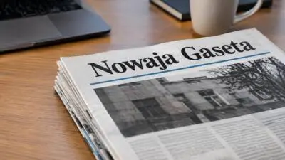 KI-generiertes Bild: Eine Zeitung mit dem Schriftzug Nowaja Gaseta liegt auf einem Holztisch neben Laptop und Tasse.