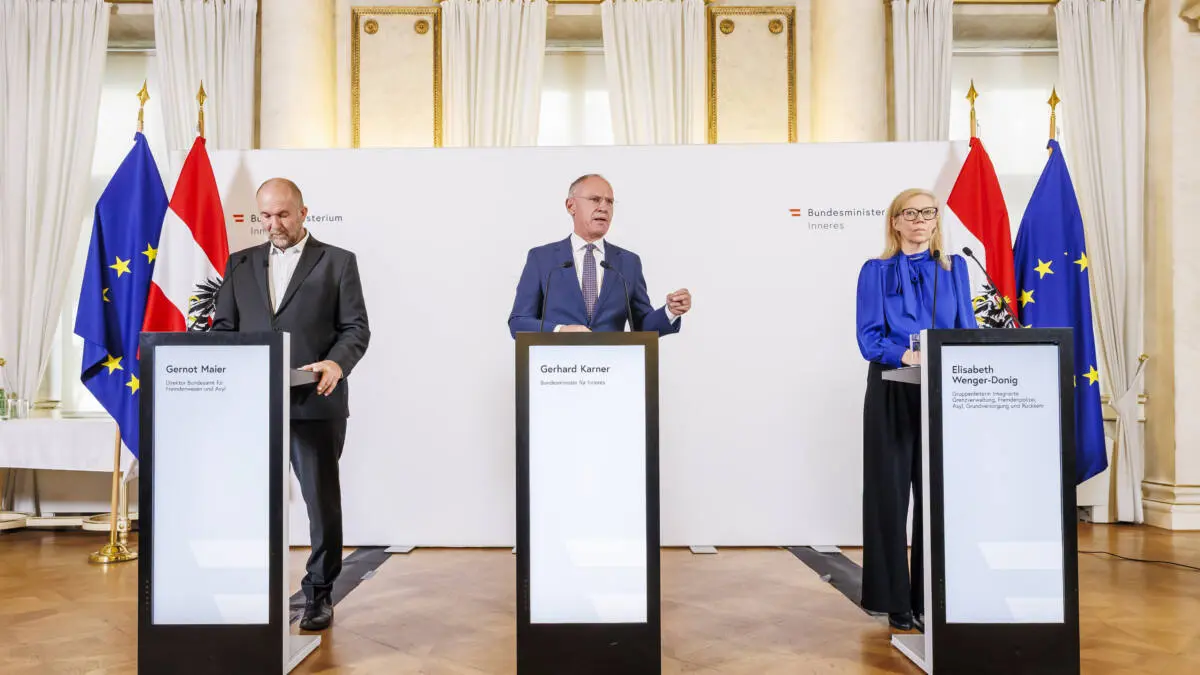 Gerhard Karner spricht an einem Rednerpult, flankiert von weiteren Personen und österreichischen sowie EU-Flaggen.