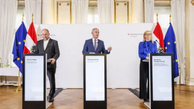 Gerhard Karner spricht an einem Rednerpult, flankiert von weiteren Personen und österreichischen sowie EU-Flaggen.