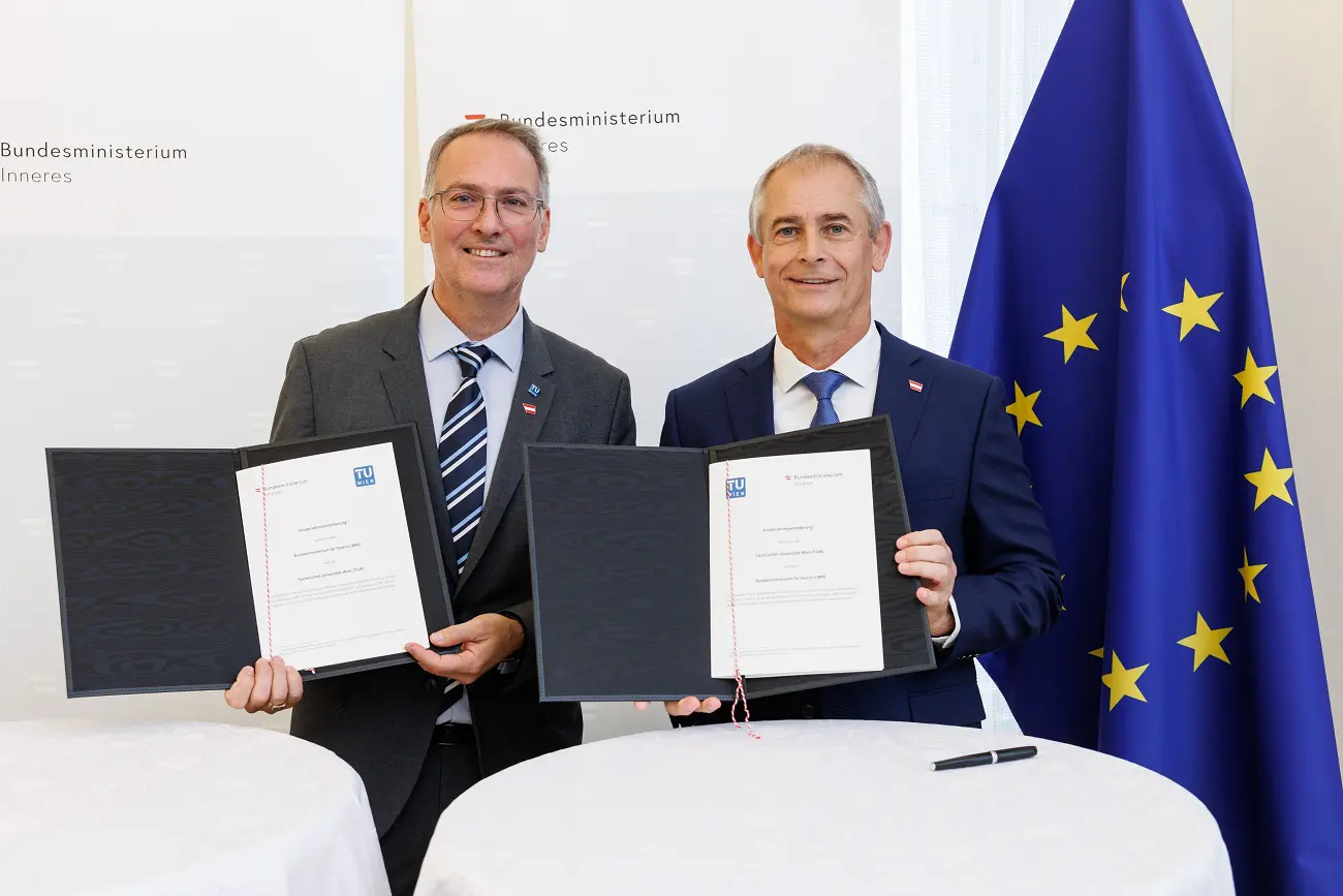 Zwei Männer in Anzügen präsentieren geöffnete Dokumentenmappen neben einer EU-Flagge.