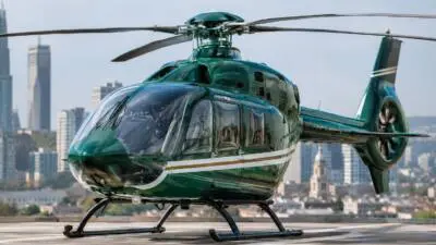 KI-Symbolbild: Ein dunkelgrüner Hubschrauber steht auf einem Dachlandeplatz vor einer Stadtansicht.