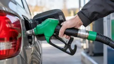 KI-generiertes Bild: Eine Hand hält eine grüne Zapfpistole am Tank eines grauen Autos.