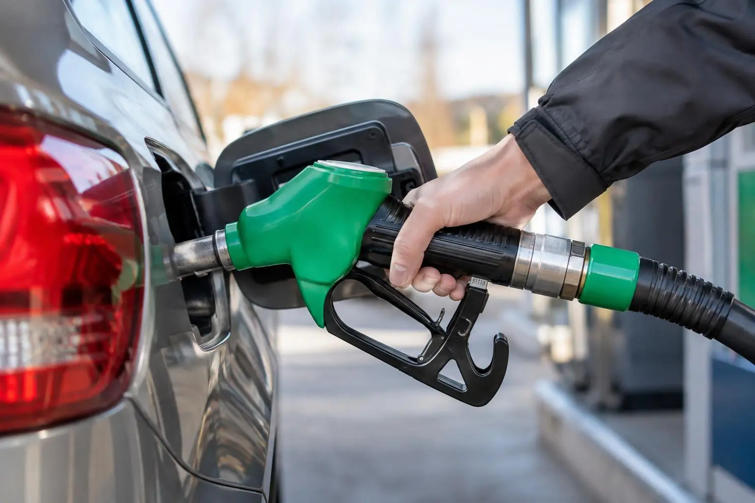 Eine Hand hält eine grüne Zapfpistole am Tank eines grauen Autos.