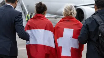 KI-Symbolbild: Zwei Frauen mit österreichischer und Schweizer Flagge vor einem Passagierflugzeug.