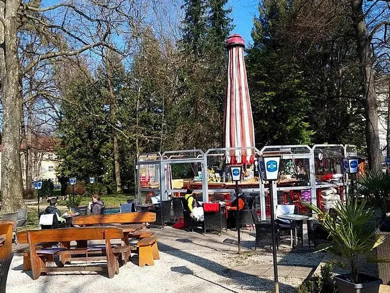 Holztische und Sitzplätze im Freien unter einem gestreiften Sonnenschirm