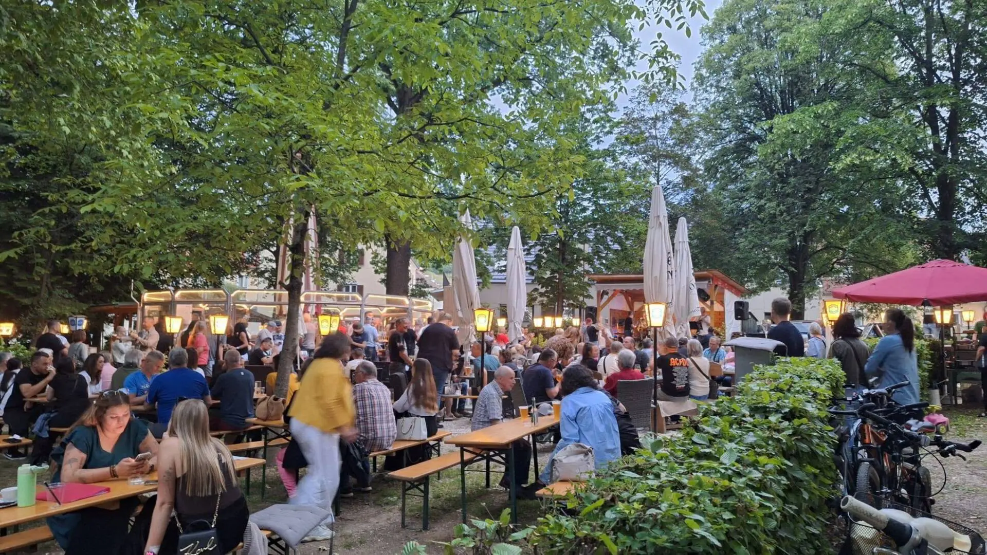 Gäste sitzen im begrünten Außenbereich eines Cafés an langen Tischen.