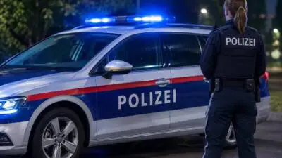 KI-generiertes Bild: Eine Polizistin steht nachts neben einem blau-weiß-roten Polizeiauto mit Blaulicht.