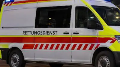 KI-generiertes Bild: Weißer Rettungswagen mit roten und gelben Streifen und eingeschaltetem Blaulicht