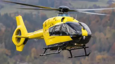 KI-Symbolbild: Ein gelber Hubschrauber vor bewaldeter Berglandschaft.