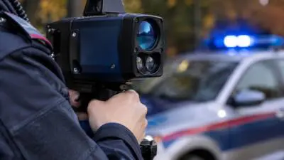 KI-Symbolbild: Eine Person hält ein Messgerät vor einem blau beleuchteten Fahrzeug.