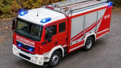 KI-Symbolbild: Ein rotes Feuerwehrfahrzeug mit Leitern steht auf einer Straße.