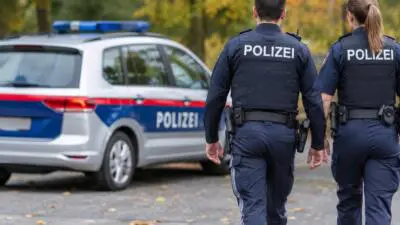 KI-generiertes Bild: Uniformierte Polizeikräfte stehen neben einem markierten Polizeiauto mit blauem Leuchtbalken.