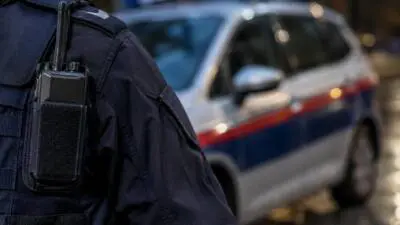 KI-Symbolbild: Eine dunkle Uniform mit Funkgerät vor einem unscharfen Auto mit rotem Streifen.