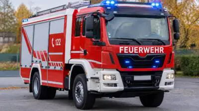 KI-Symbolbild: Ein rotes Feuerwehrfahrzeug mit eingeschaltetem Blaulicht steht auf einer Straße.