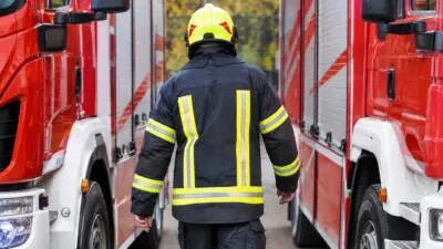KI-Symbolbild: Eine Einsatzkraft mit gelbem Helm zwischen roten Feuerwehrfahrzeugen.