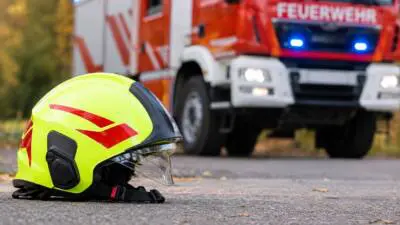 KI-generiertes Bild: Ein leuchtgelber Feuerwehrhelm liegt vor einem roten Feuerwehrfahrzeug mit Blaulicht.
