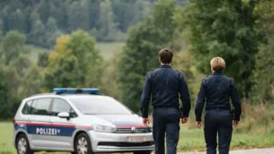 KI-Symbolbild zum Thema Verkehrsunfall: Polizeibeamte gehen auf einem Landweg neben einem Streifenwagen.