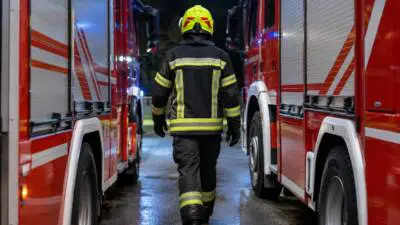 KI-generiertes Bild: Eine Person in dunkler Schutzkleidung geht zwischen roten Fahrzeugen.