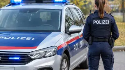 KI-generiertes Bild: Eine uniformierte Person steht neben einem blau-weißen Fahrzeug mit blauem Signallicht.