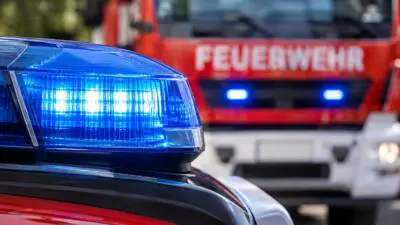 KI-Symbolbild: Ein blaues Warnlicht auf einem roten Fahrzeug vor einem Feuerwehrfahrzeug.
